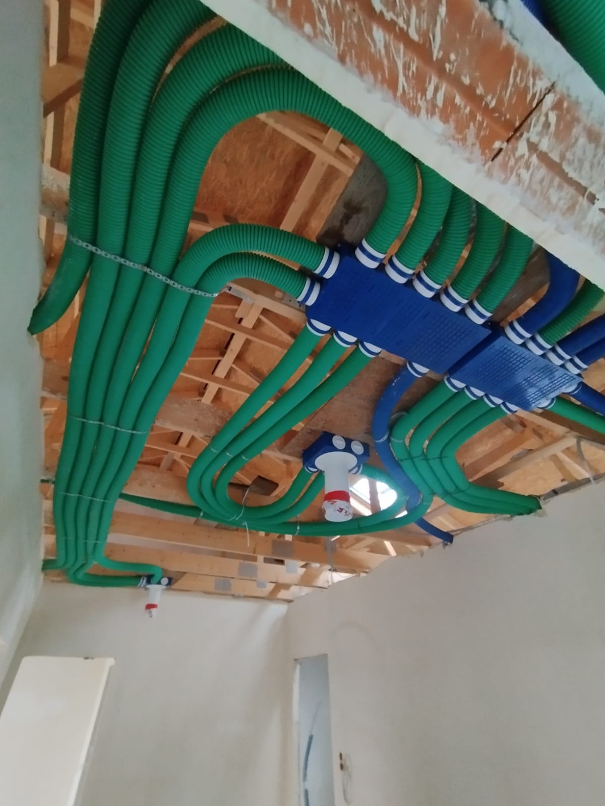 Zielone i niebieskie rury rekuperacji zamontowane pod drewnianą konstrukcją stropu, widoczne złącza i elementy instalacji.