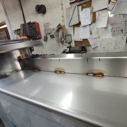 Ślusarskie usługi mobilne Łukasz Piekielniak - Spoina na metalowej konstrukcji w warsztacie, widoczne ślady po spawaniu i narzędzia w tle.