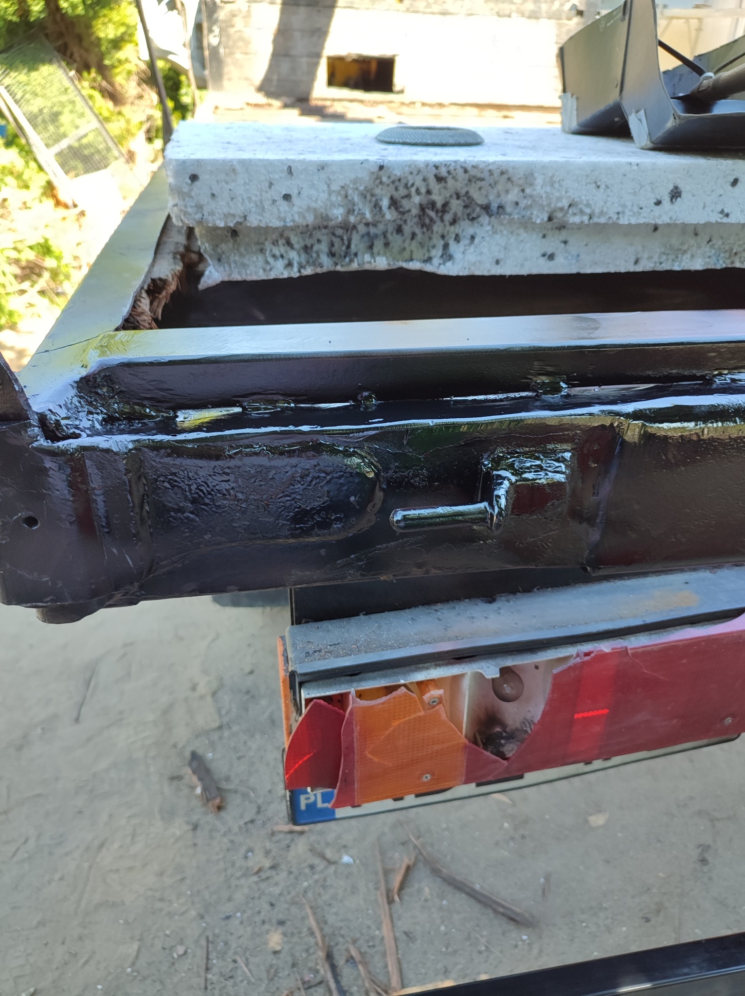 Fragment ramy przyczepy, świeżo pomalowana na czarno, widoczne ślady niedokładnego malowania i uszkodzony reflektor.