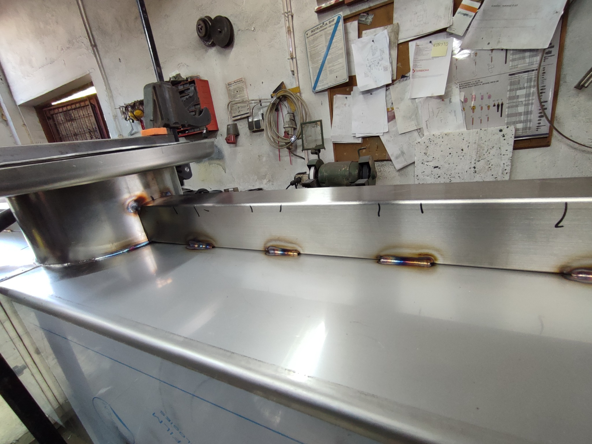 Spoina na metalowej konstrukcji w warsztacie, widoczne ślady po spawaniu i narzędzia w tle.