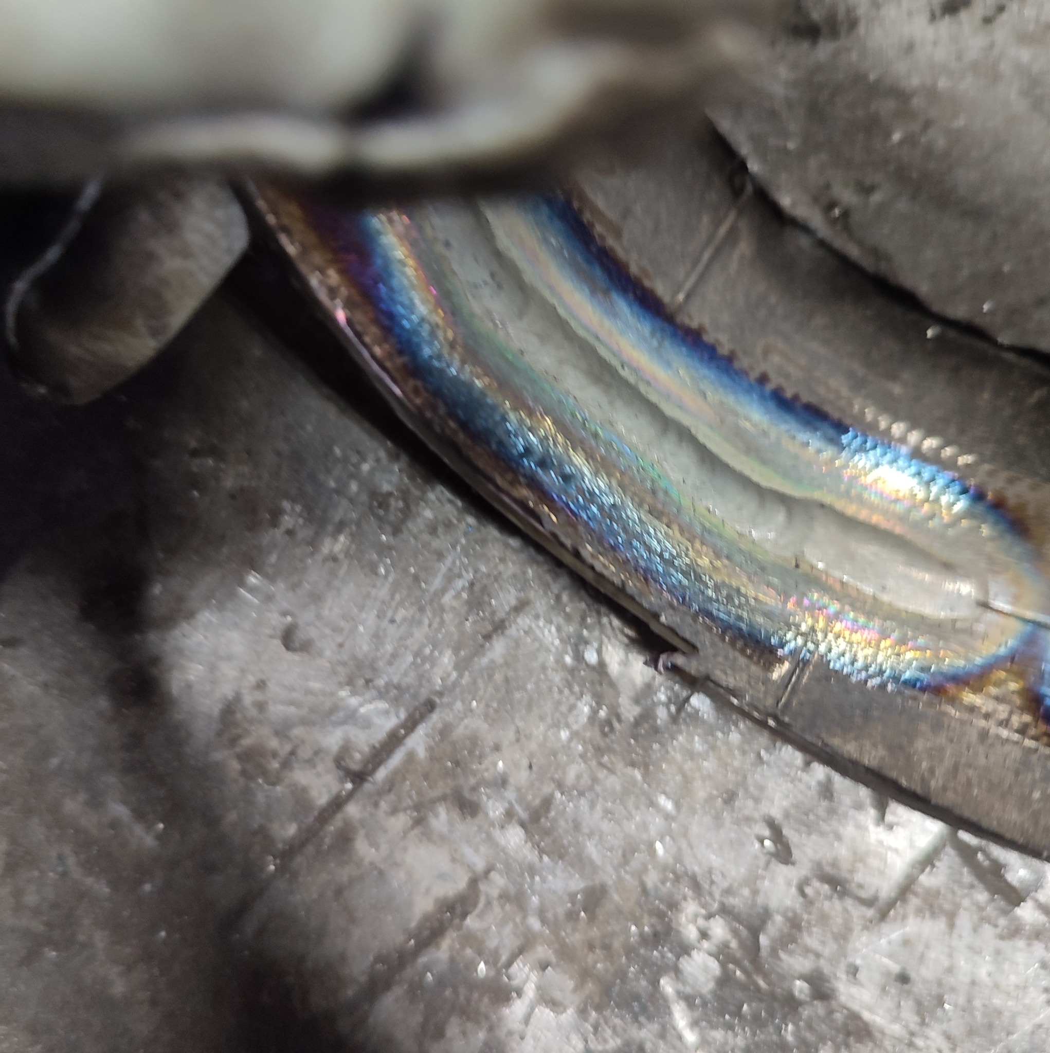 Zbliżenie na spawany, zakrzywiony element metalowy z widocznymi kolorami hartowania na spoinie.