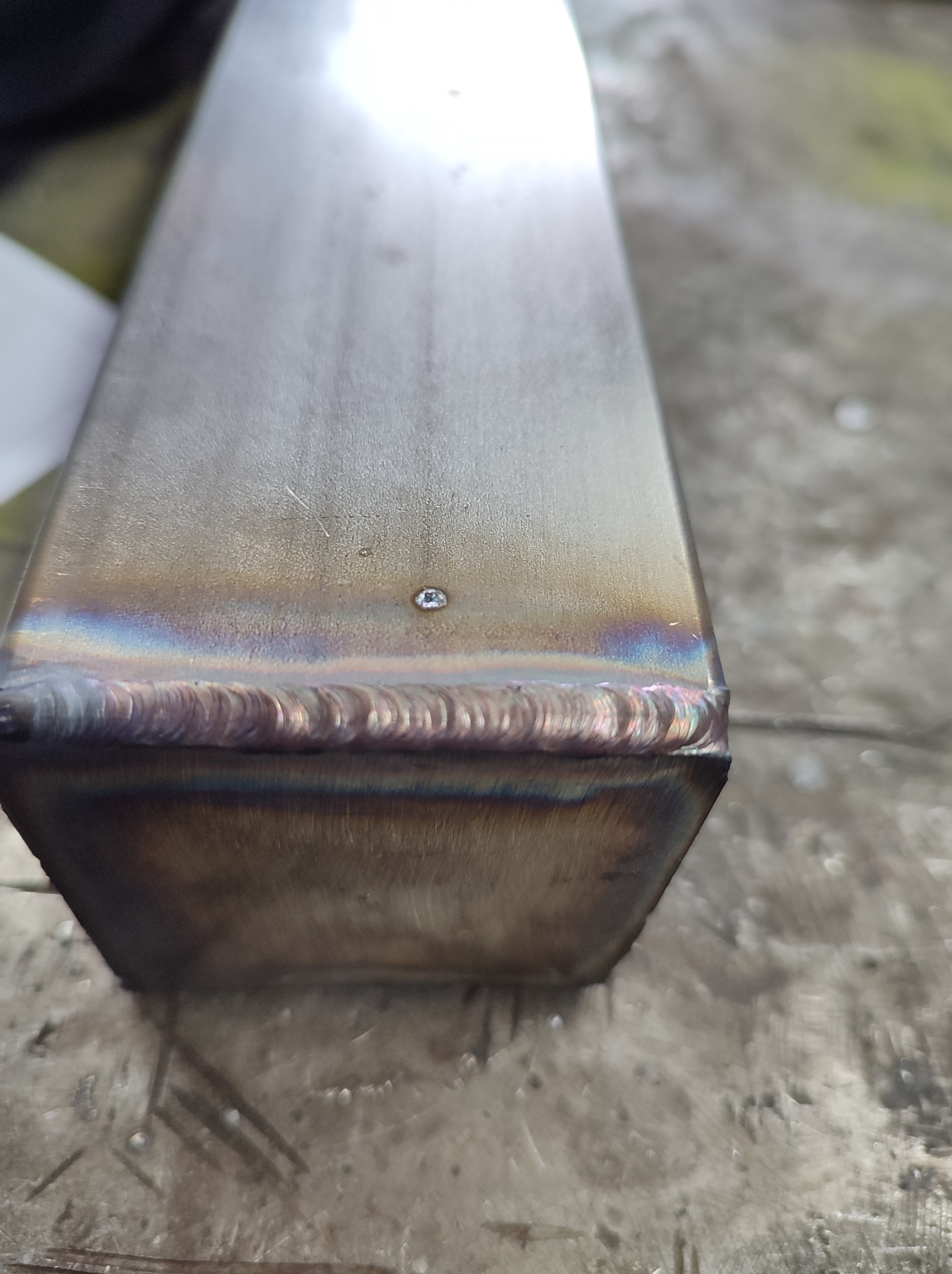 Detale spoiny na krawędzi metalowego profilu o przekroju prostokątnym, widoczne tęczowe przebarwienia termiczne.