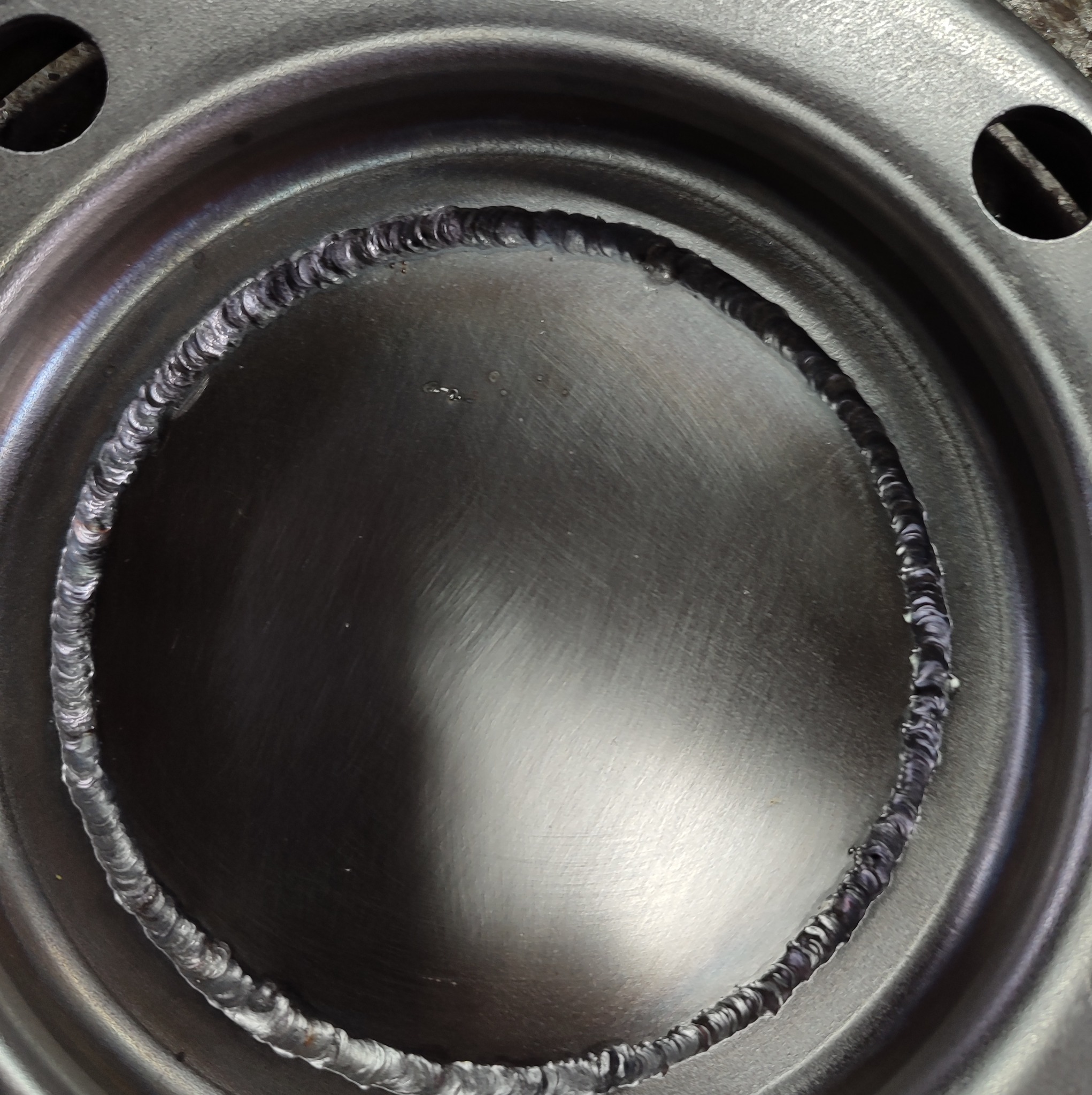 Metalowy element z widocznym spawem po okręgu, widoczne ślady obróbki i dwa otwory montażowe.