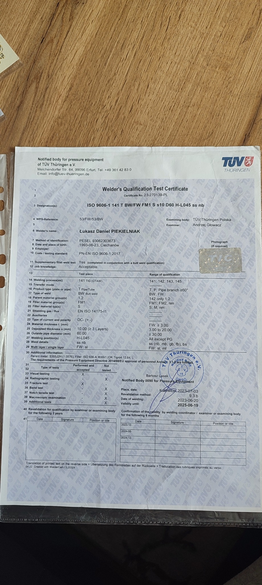 Skan certyfikatu kwalifikacji spawacza TÜV Thüringen Polska, z danymi Łukasza Daniela Piekielniaka, potwierdzający zgodność z normą ISO 9606-1, z pieczęcią i tabelami wpisów o rewalidacji.