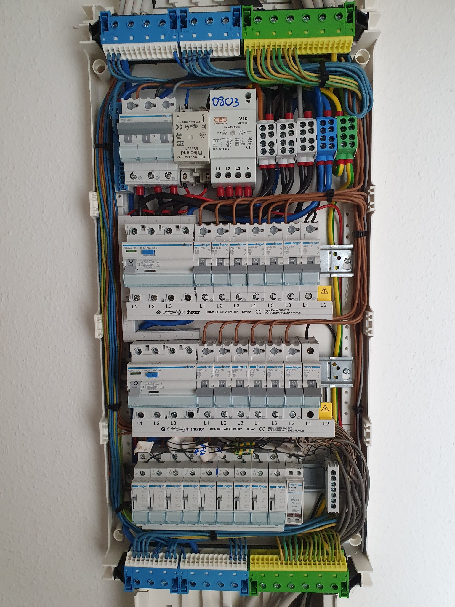 Otwarta skrzynka rozdzielcza z zainstalowanymi zabezpieczeniami Hager, widoczne bezpieczniki, wyłączniki różnicowoprądowe oraz kolorowe przewody elektryczne.