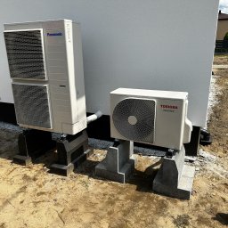 AMPERE SPÓŁKA Z OGRANICZONĄ ODPOWIEDZIALNOŚCIĄ - Dwie zewnętrzne jednostki klimatyzacji: Panasonic ustawiona pionowo i Toshiba Inverter, obie na betonowych podstawach przy białej ścianie budynku, widoczna pompa próżniowa w rogu.
