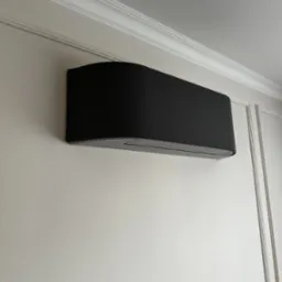 Czarny klimatyzator ścienny w nowoczesnym wnętrzu z dekoracyjną listwą przysufitową i panelami ściennymi.