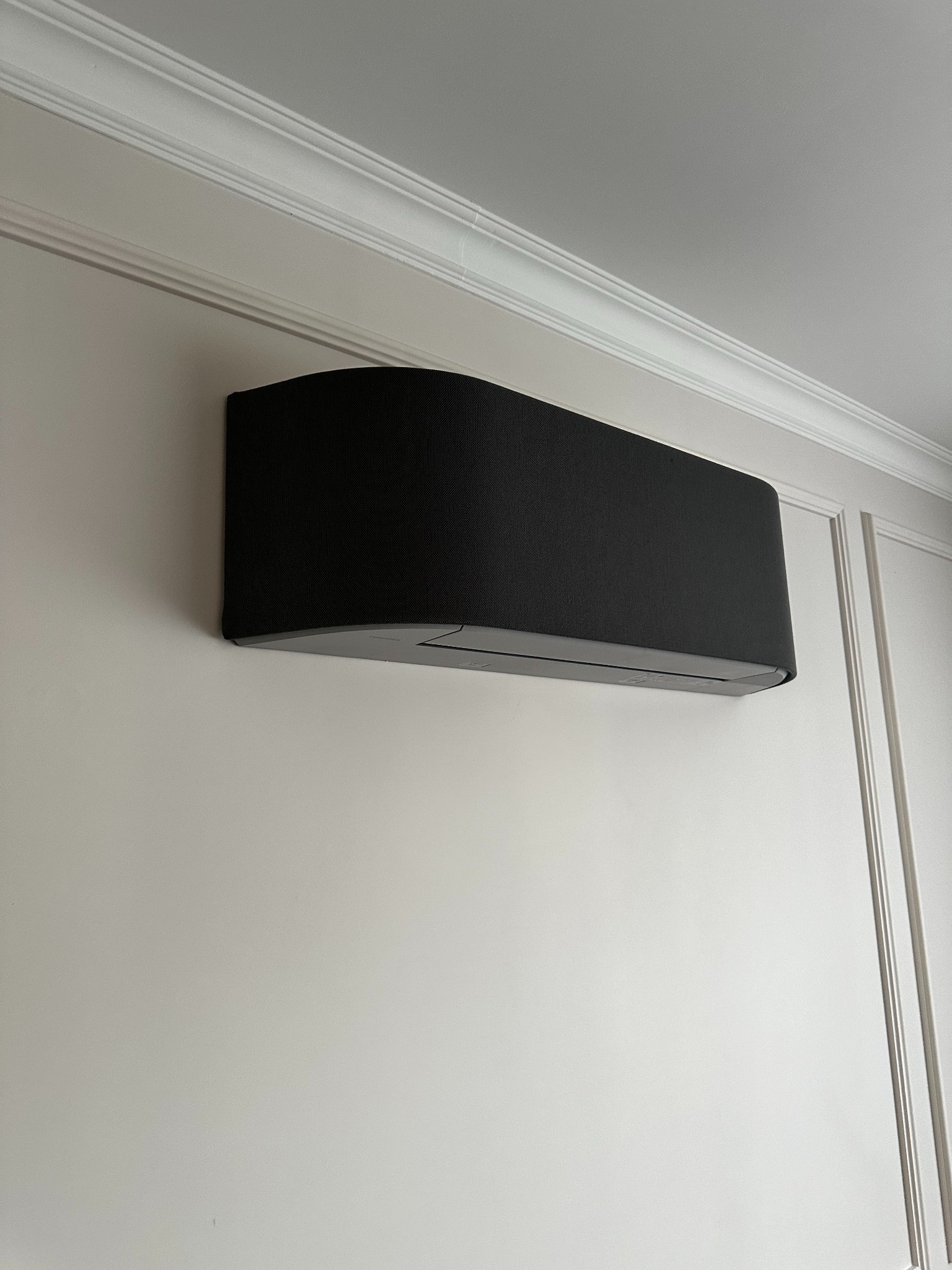 Czarny klimatyzator ścienny w nowoczesnym wnętrzu z dekoracyjną listwą przysufitową i panelami ściennymi.