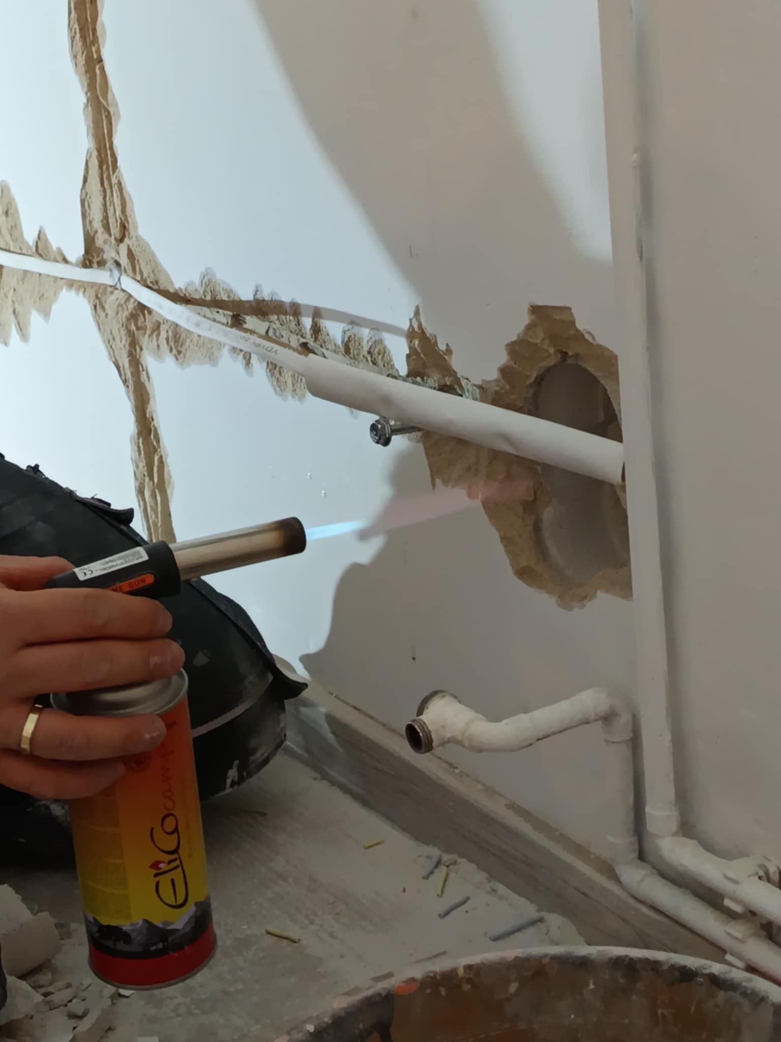 Prace instalacyjne w Malborku: lutowanie rur instalacji wodnej palnikiem gazowym w miejscu uszkodzenia ściany.