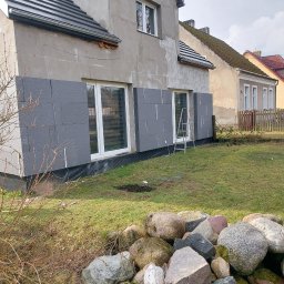 Mar bud - Dom w trakcie docieplania elewacji styropianem grafitowym, widoczne fragmenty ocieplenia przy oknach, drabina oparta o ścianę, na pierwszym planie kamienie.