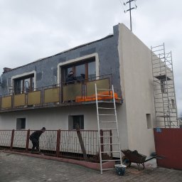 Mar bud - Ocieplanie elewacji dwupiętrowego budynku z balkonem, widoczne rusztowanie, drabiny, styropianowe płyty i pracownicy w trakcie montażu, pochmurne niebo w tle.