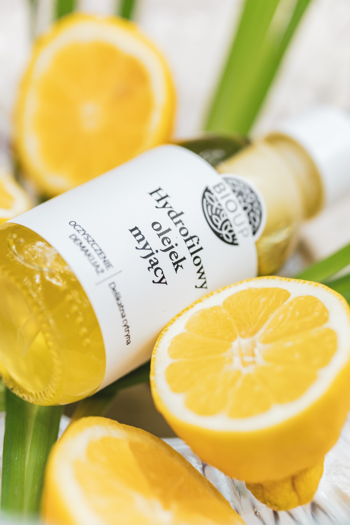 Butelka hydrofilowego olejku myjącego marki Bioup, otoczona połówkami cytryny i zielonymi liśćmi, prezentowana w zbliżeniu.