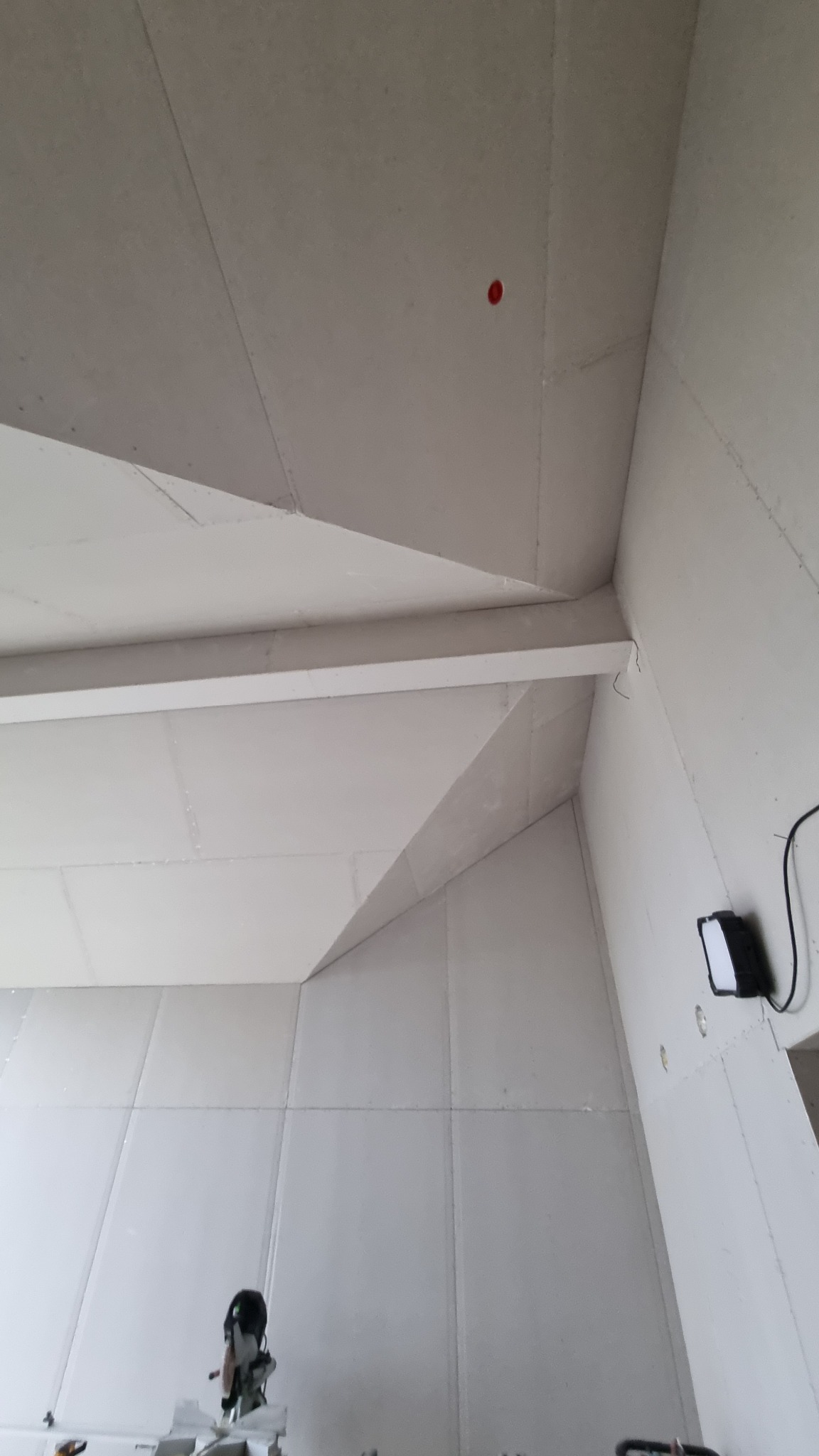 Wnętrze w trakcie montażu płyt gipsowo-kartonowych na ścianach i suficie, widoczna konstrukcja nośna i lampa robocza.