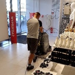 ANS Clean Craft Sprzątanie Profesjonalne i Ozonowanie - Pracownik w sklepie czyści podłogę za pomocą maszyny czyszczącej. Widoczny asortyment sklepowy i szyld 'Wyprzedaż'.