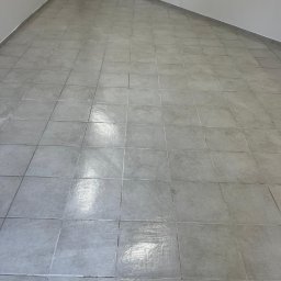 ANS Clean Craft Sprzątanie Profesjonalne i Ozonowanie - Wnętrze z szarymi płytkami podłogowymi ułożonymi w kwadraty, widoczne ślady po umyciu, ściany jasne, minimalistyczne wykończenie.