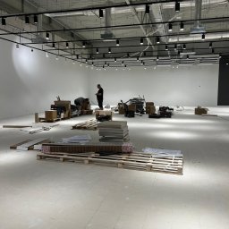 ANS Clean Craft Sprzątanie Profesjonalne i Ozonowanie - Wnętrze sklepu Sinsay w galerii Wyszków w trakcie sprzątania po remoncie. Widoczne palety, kartony i dwie osoby sprzątające. Oświetlenie sufitowe.