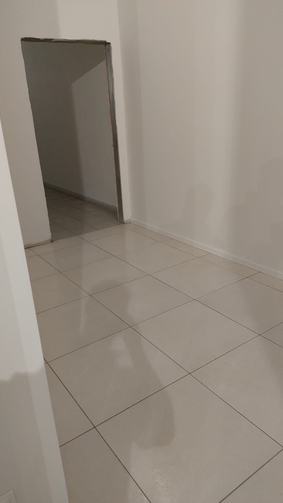 Wnętrze po remoncie: jasne płytki podłogowe i świeżo pomalowane ściany w odcieniach bieli. Widoczne przejście do kolejnego pomieszczenia.