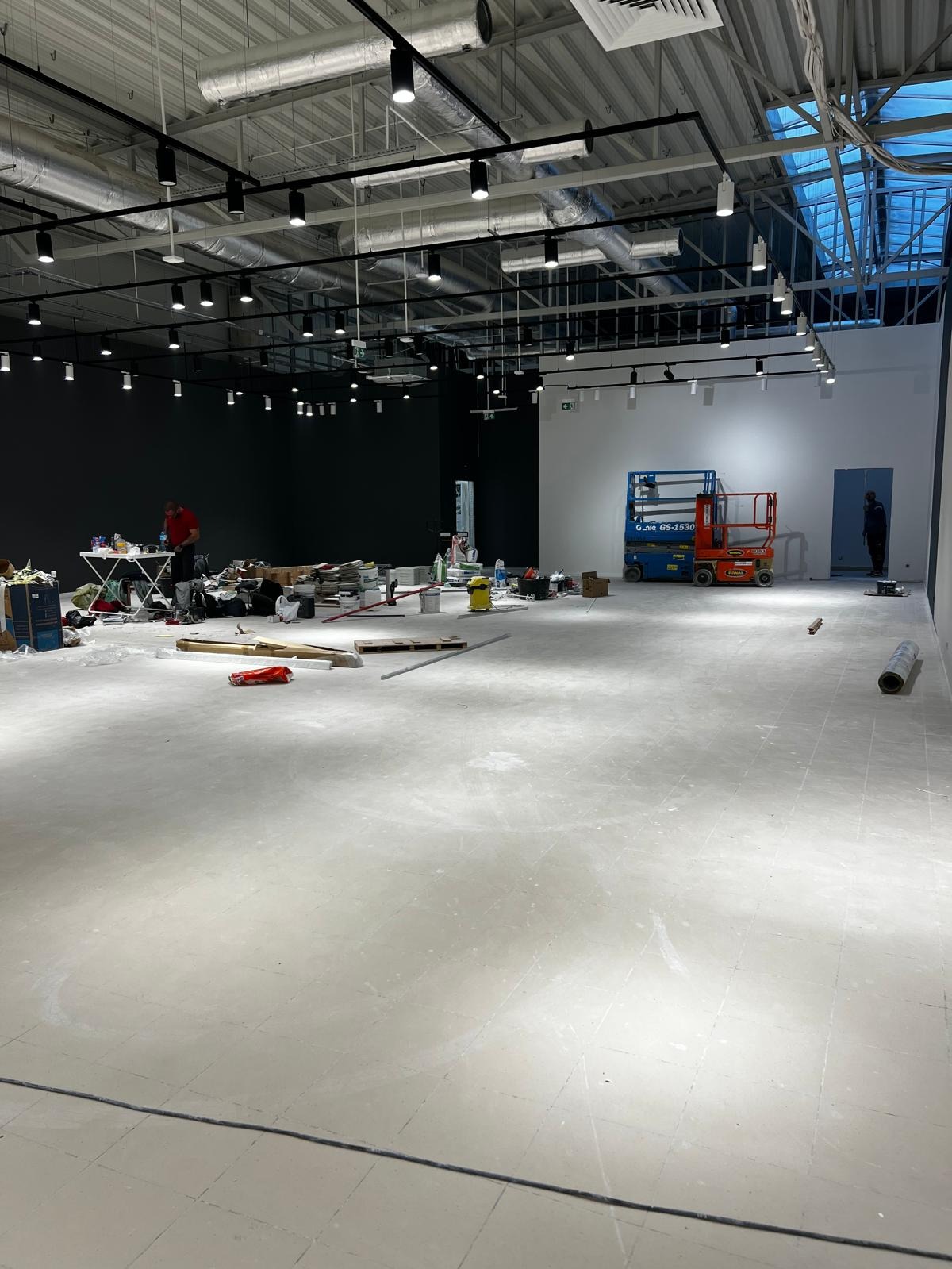 Wnętrze sklepu Sinsay w galerii Wyszków po remoncie. Widoczne podnośniki, materiały budowlane i ekipa sprzątająca. Oświetlenie sufitowe i surowa podłoga.