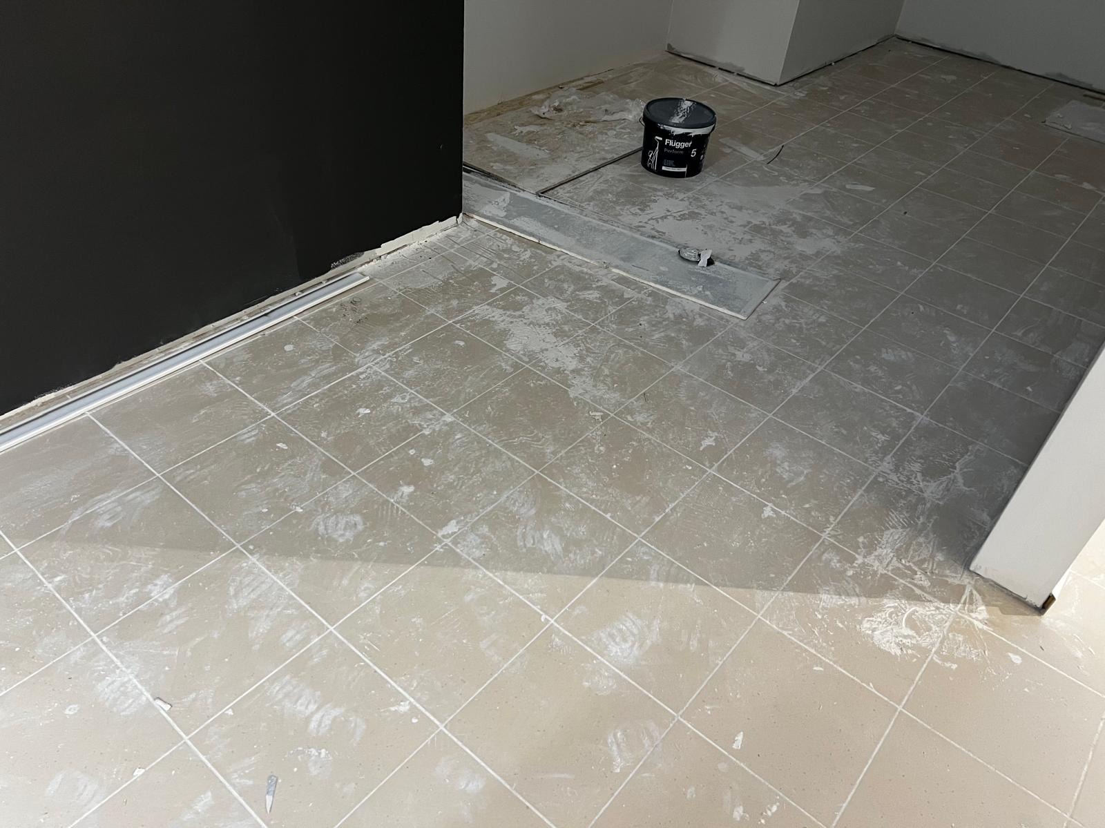 Podłoga w trakcie sprzątania po remoncie, widoczne płytki pokryte zabrudzeniami, wiadro z farbą w tle. Ujęcie z góry, blisko czarnej ściany.