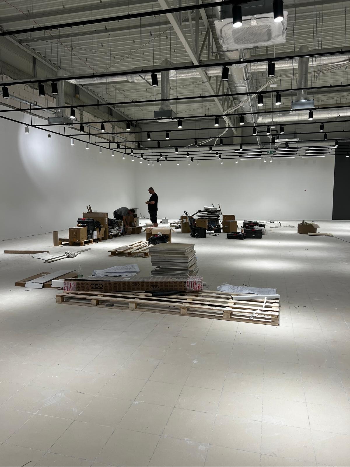 Wnętrze sklepu Sinsay w galerii Wyszków w trakcie sprzątania po remoncie. Widoczne palety, kartony i dwie osoby sprzątające. Oświetlenie sufitowe.