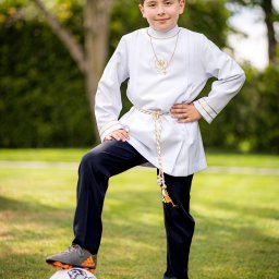 Pan Aparacik Dawid Kubica - Chłopiec w stroju komunijnym z medalikiem i sznurem, stojący z nogą na piłce nożnej w Siewierzu, na tle zielonego ogrodu.