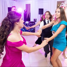 Pan Aparacik Dawid Kubica - Roztańczona grupa młodych ludzi w eleganckich strojach, bawiąca się na parkiecie podczas imprezy. W tle dekoracje kwiatowe i efekty świetlne.