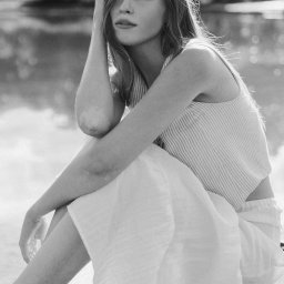 suzanephoto - Portret w czerni i bieli: młoda kobieta siedzi z ręką na głowie, w tle rozmyte jezioro i drzewa.