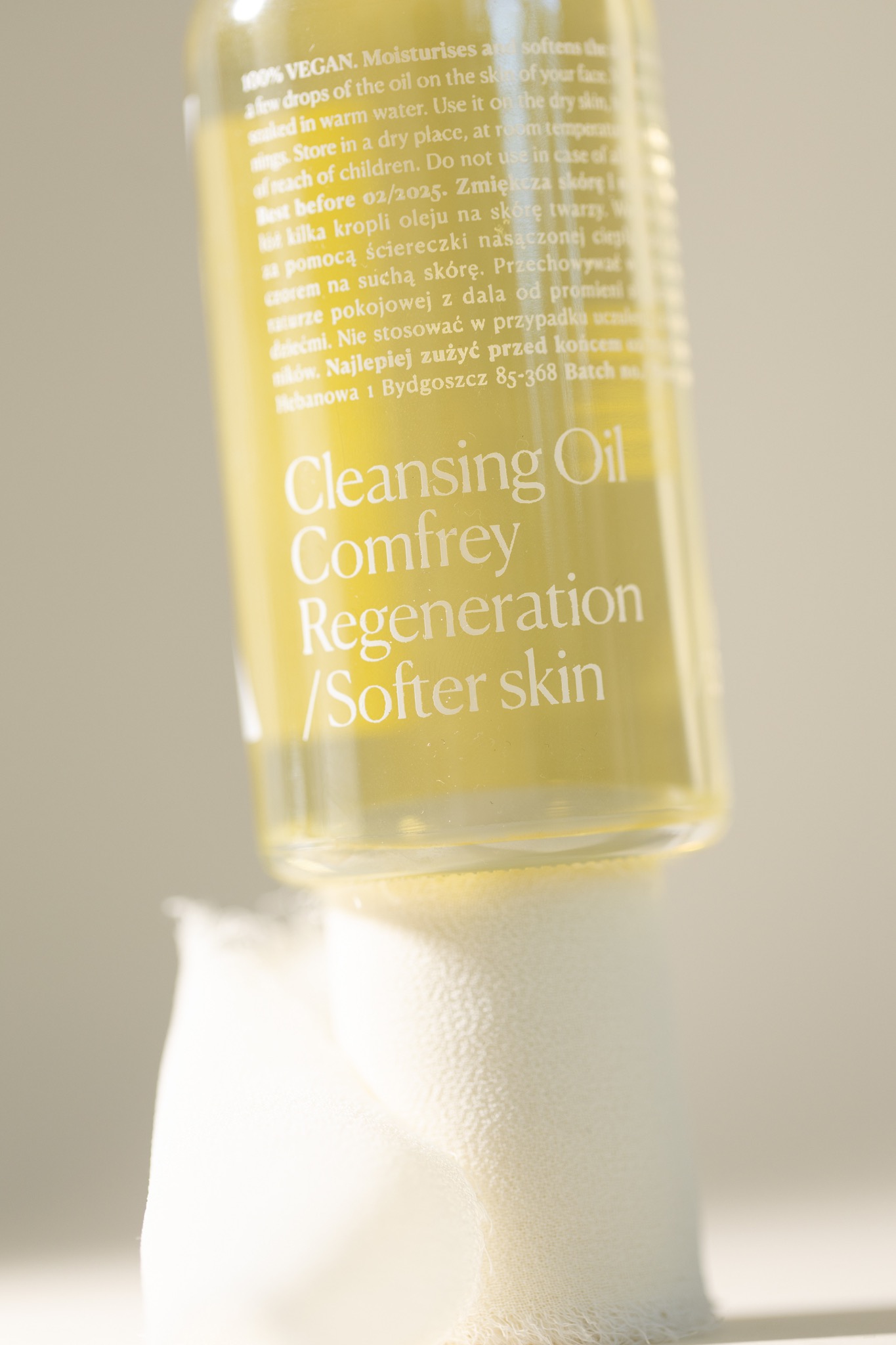 Butelka wegańskiego olejku do demakijażu Cleansing Oil Comfrey Regeneration / Softer skin, ustawiona na białej, miękkiej ściereczce, z widocznymi napisami o właściwościach nawilżających...