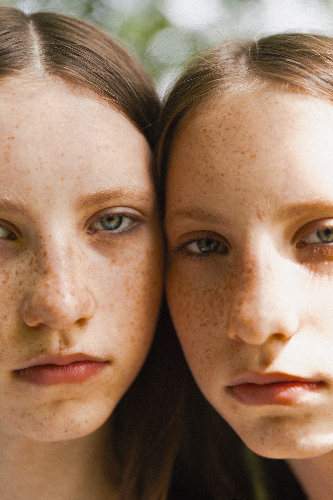 Portret dwóch młodych dziewczyn z piegami, blisko siebie, zamyślone spojrzenie, naturalne światło.
