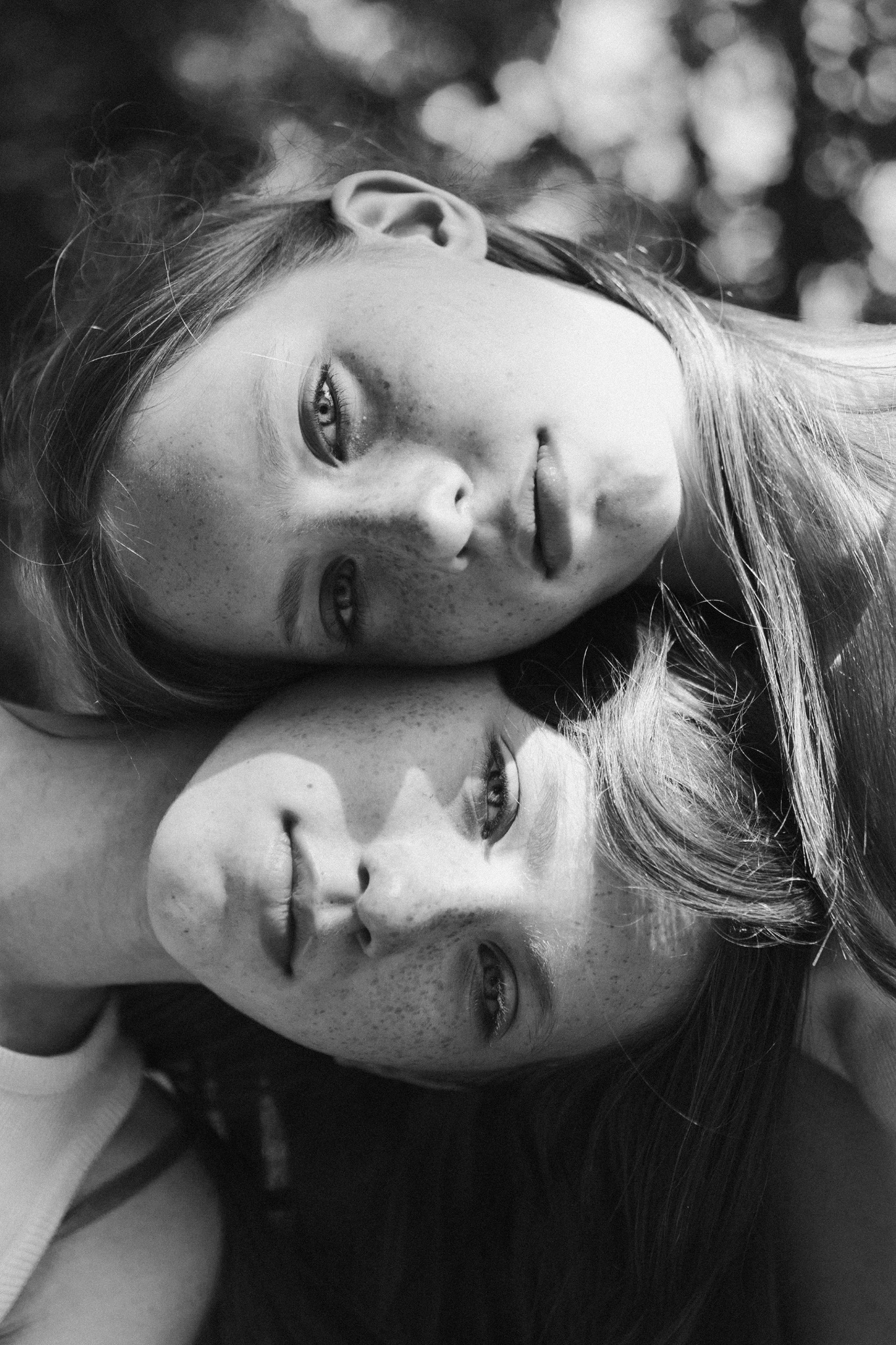 Czarno-białe portretowe zbliżenie dwóch dziewcząt z piegami, leżących głowami blisko siebie, z zamyślonym spojrzeniem w obiektyw.