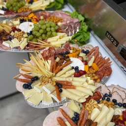 Adam Oberda - Food Group - Kilka aluminiowych tac z różnorodnymi przekąskami: sery, wędliny, owoce (winogrona, borówki, truskawki) i orzechy ułożone kompozycyjnie na przyjęcie.