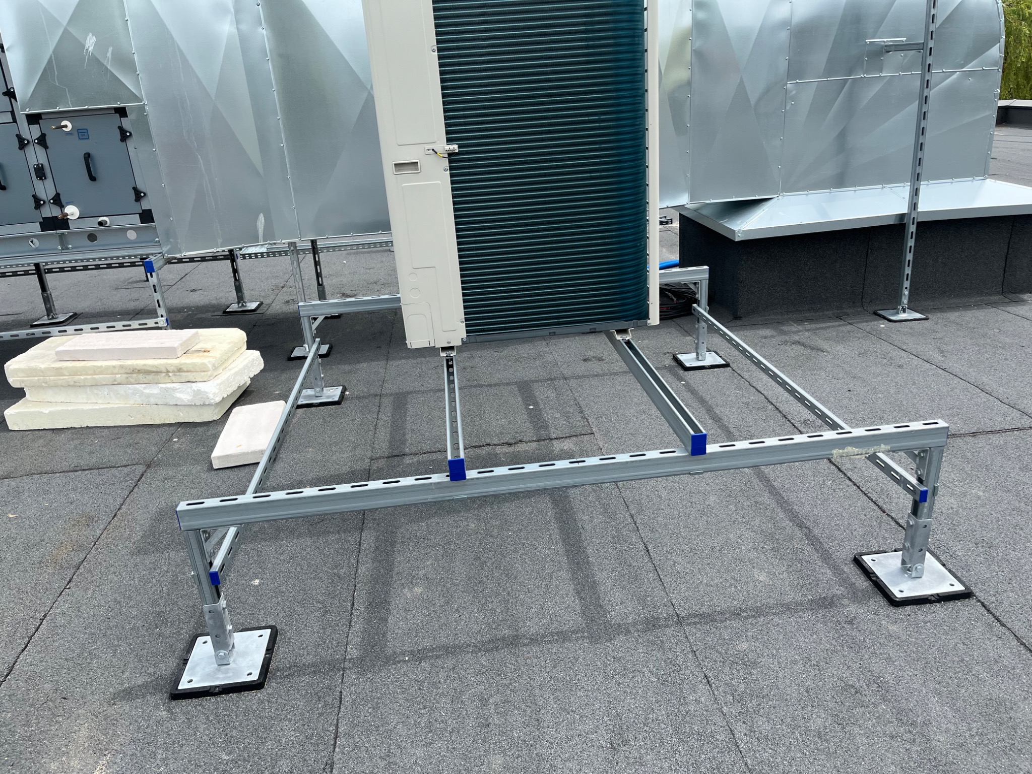 Montaż jednostki zewnętrznej klimatyzacji na dachu budynku. Widoczne metalowe konstrukcje wsporcze i elementy instalacji wentylacyjnej. Dach pokryty papą.