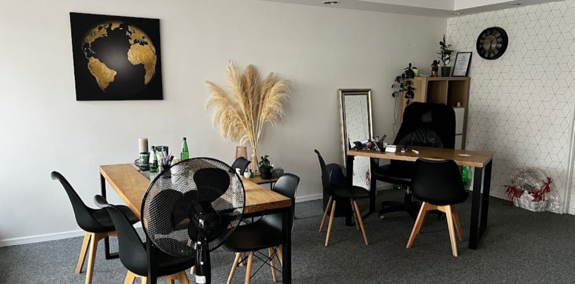 Nowoczesne biuro z drewnianym stołem, czarnymi krzesłami, dekoracjami z pampasowej trawy, obrazem z motywem złotej mapy świata i biurkiem z komputerem w tle.