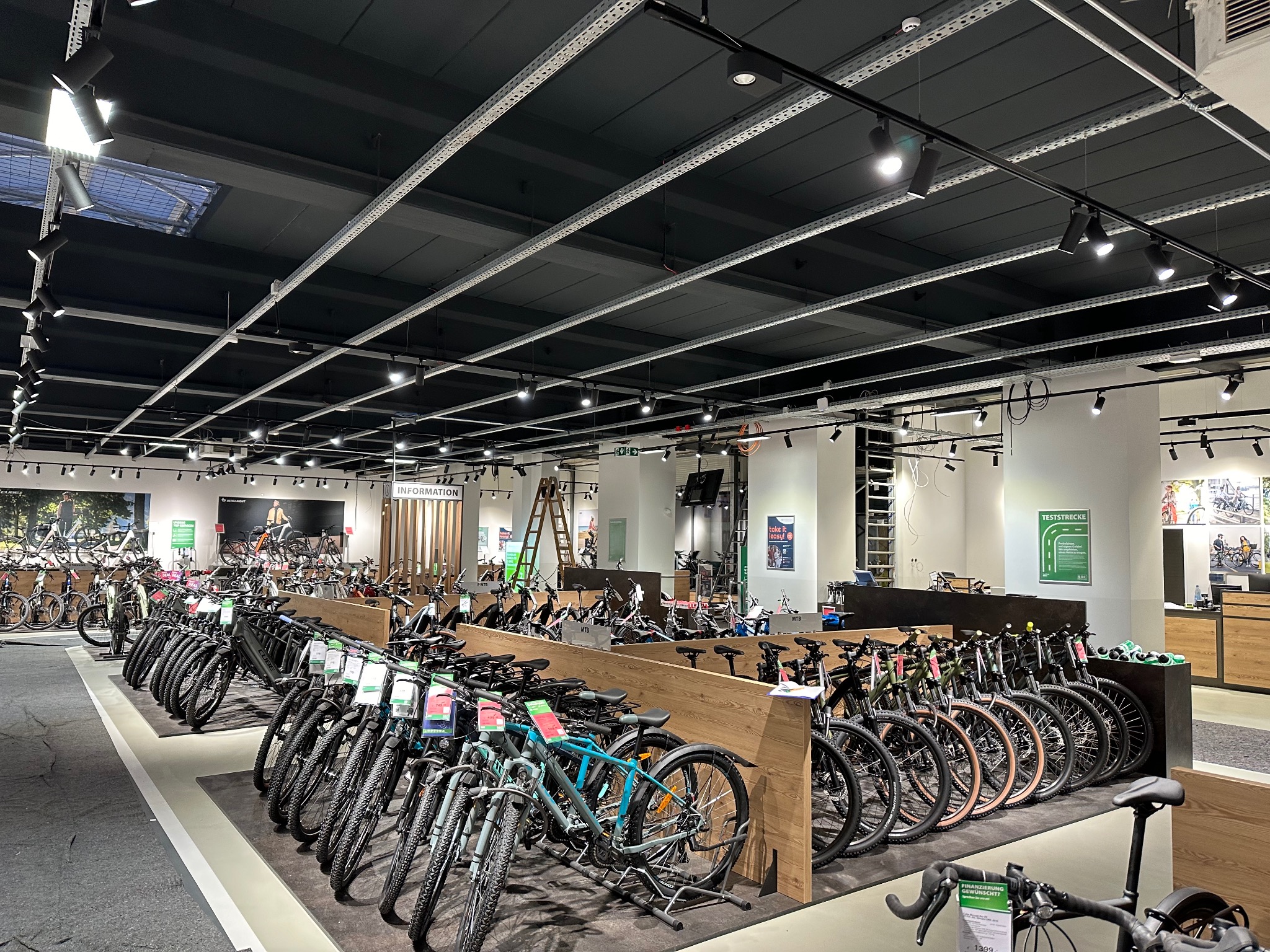 Wnętrze sklepu rowerowego z rzędami rowerów, widoczne metalowe szyny pod sufitem z zamontowanymi punktowymi reflektorami.