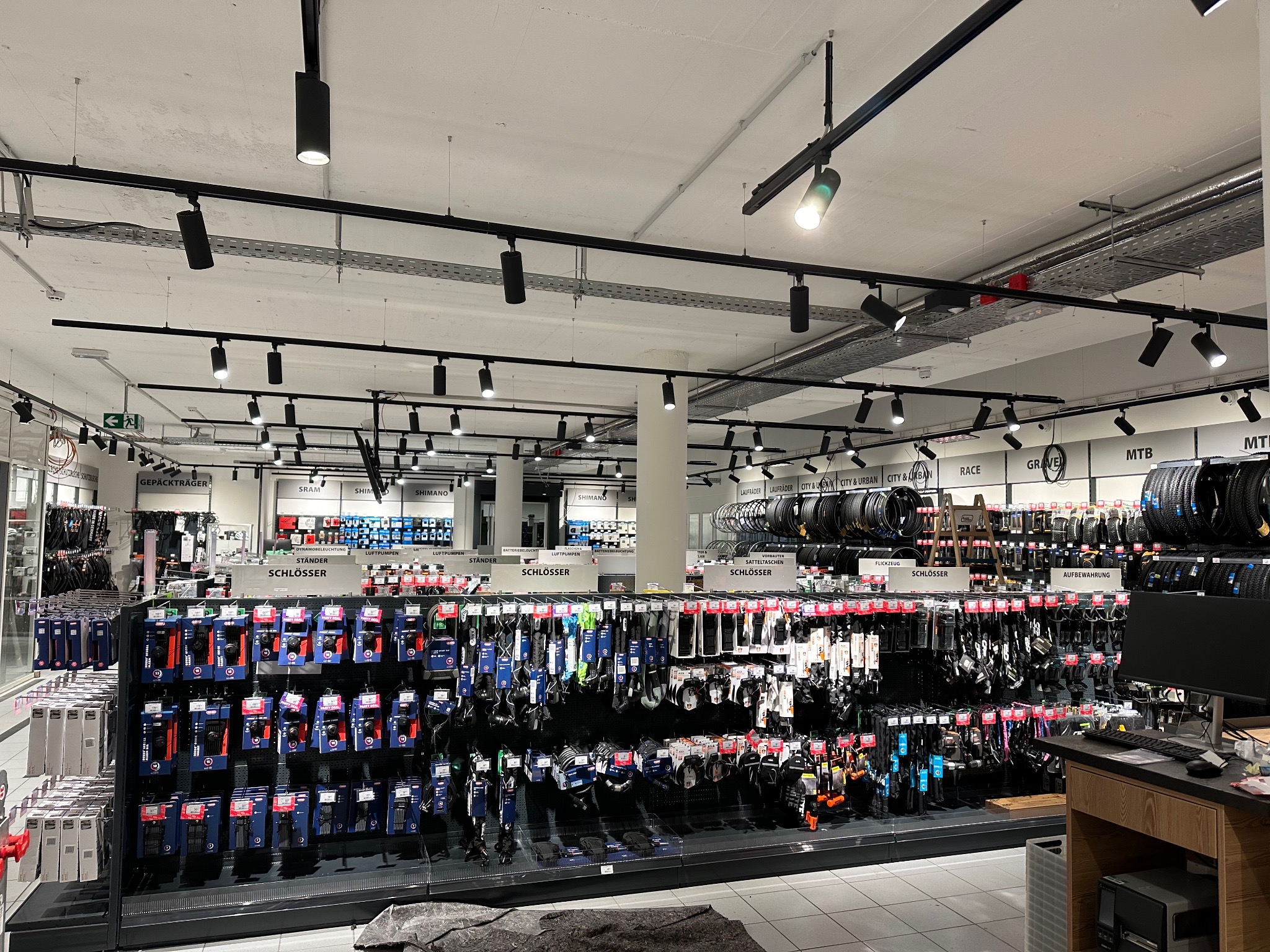 Wnętrze sklepu rowerowego z widocznym systemem szynoprzewodów oświetleniowych z reflektorami punktowymi w kolorze czarnym, oświetlającymi ekspozycję akcesoriów rowerowych
