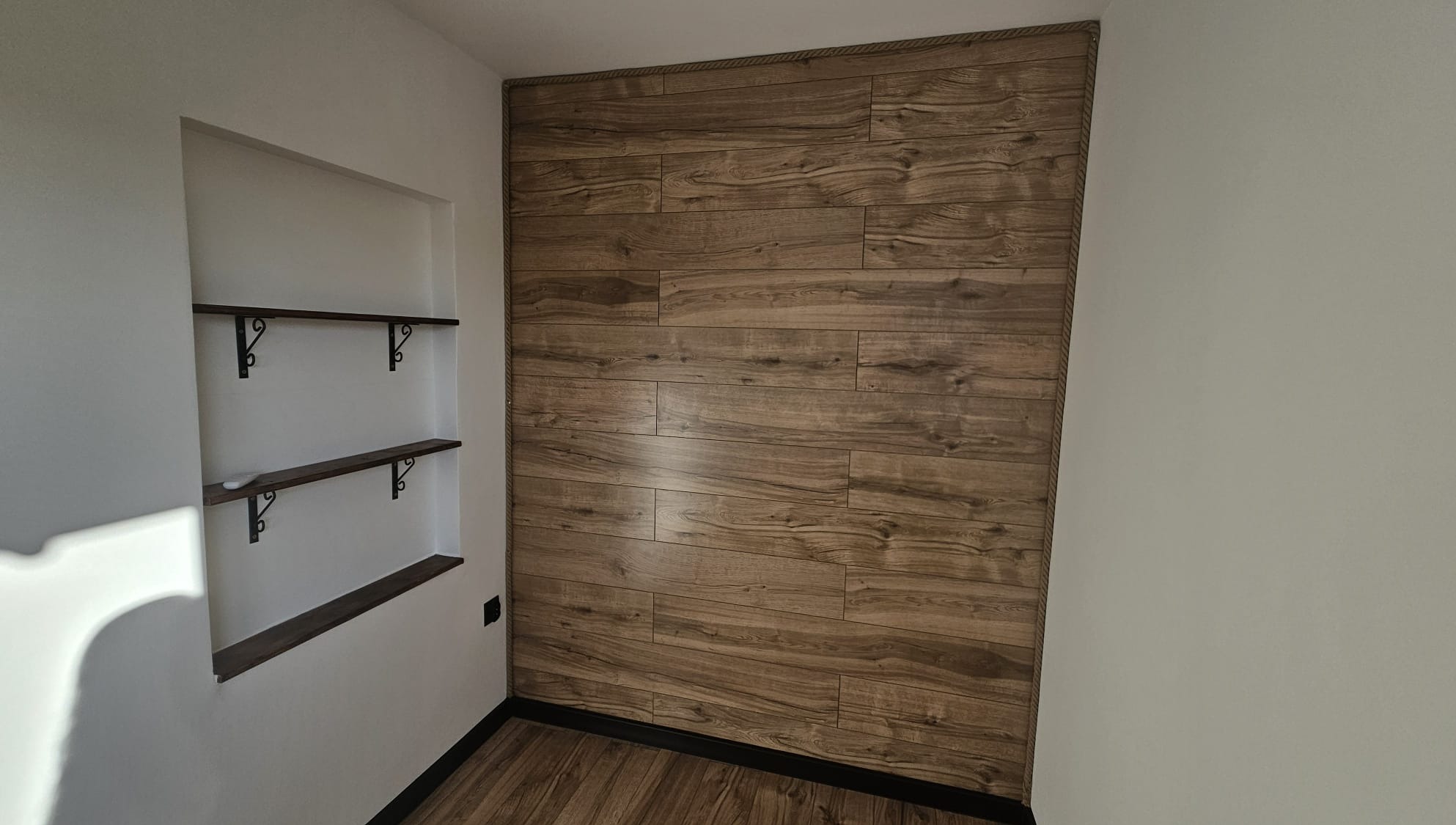 Wykończone wnętrze: ściana z paneli drewnopodobnych, wnęka z półkami na ozdobnych wspornikach, podłoga z paneli. Estetyczne detale.