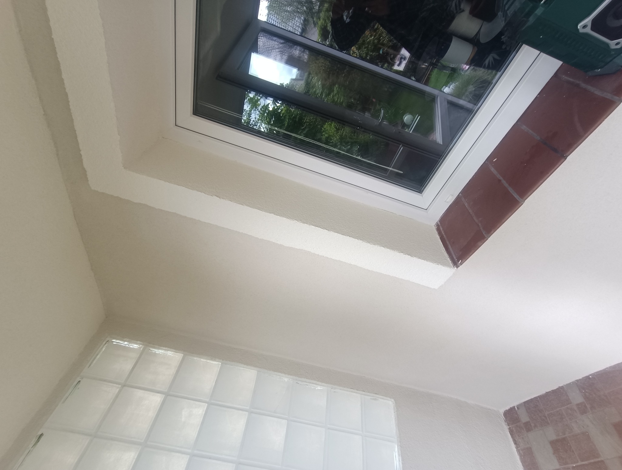 Białe ściany po szpachlowaniu i malowaniu, widoczne okno dachowe z widokiem na zieleń oraz luksfery w dolnej części ściany. Wykończenie wnętrza.