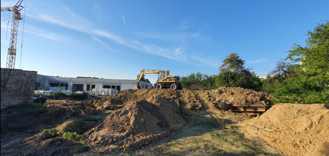 Żółta koparka CAT na wzgórzu ziemi podczas prac ziemnych na tle budowanego budynku i błękitnego nieba.