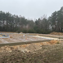 TipTopDom.pl - Zbrojona płyta fundamentowa z izolacją obwodową na działce z widocznym lasem w tle, przygotowana do dalszych prac budowlanych.