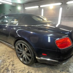 ŻELAZO TEAM SPÓŁKA Z OGRANICZONĄ ODPOWIEDZIALNOŚCIĄ - Granatowy kabriolet Bentley Continental z czarnym dachem, po myciu, widoczny z tyłu pod kątem, na mokrej posadzce warsztatu z oświetleniem jarzeniowym.