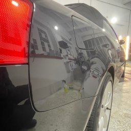 ŻELAZO TEAM SPÓŁKA Z OGRANICZONĄ ODPOWIEDZIALNOŚCIĄ - Szary samochód w warsztacie w Warszawie, widoczne ślady po polerowaniu lakieru i odbicie okien w karoserii.