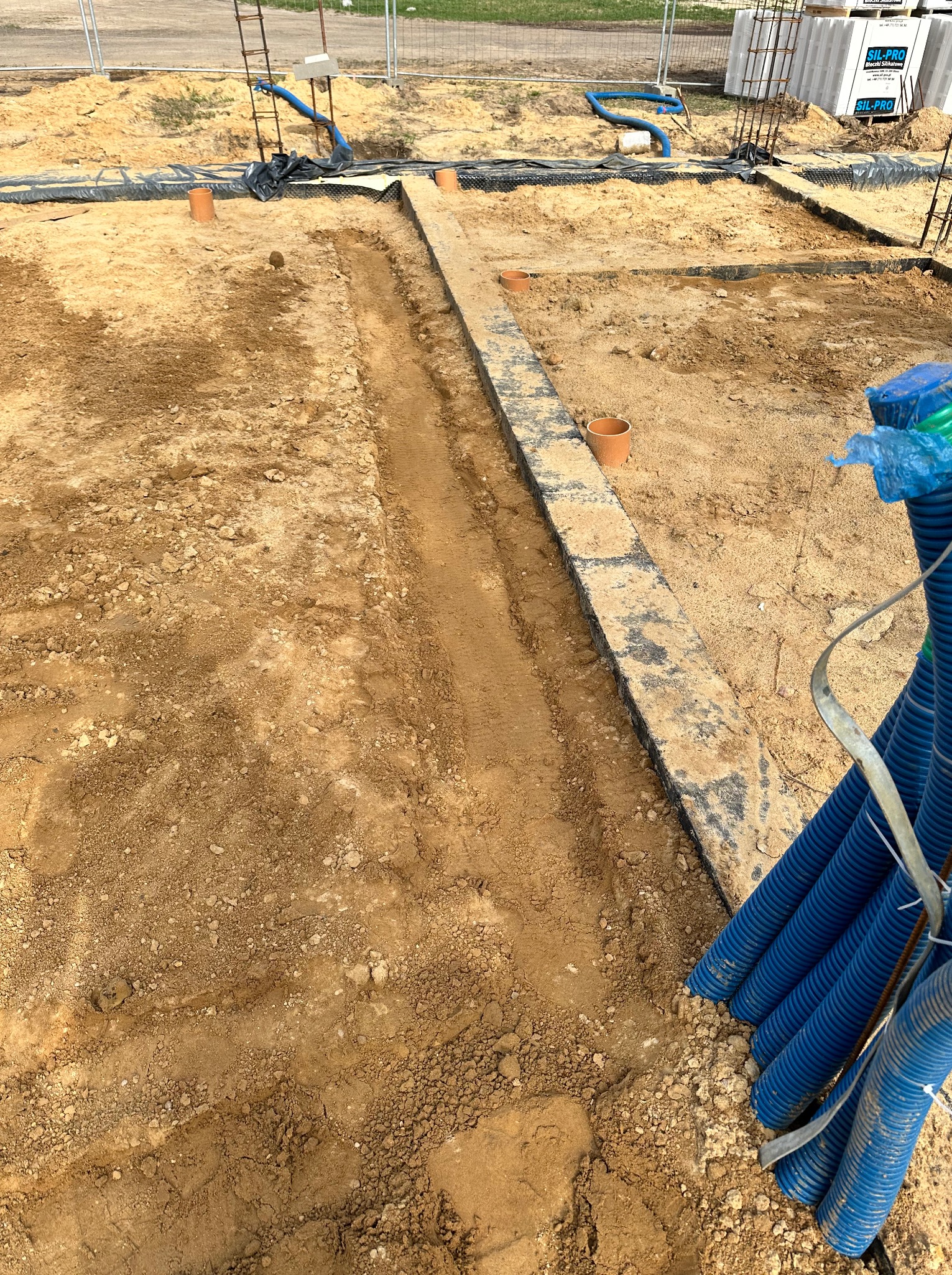 Przygotowanie wykopu pod fundamenty z ułożonymi przepustami kablowymi w niebieskiej karbowanej rurze.