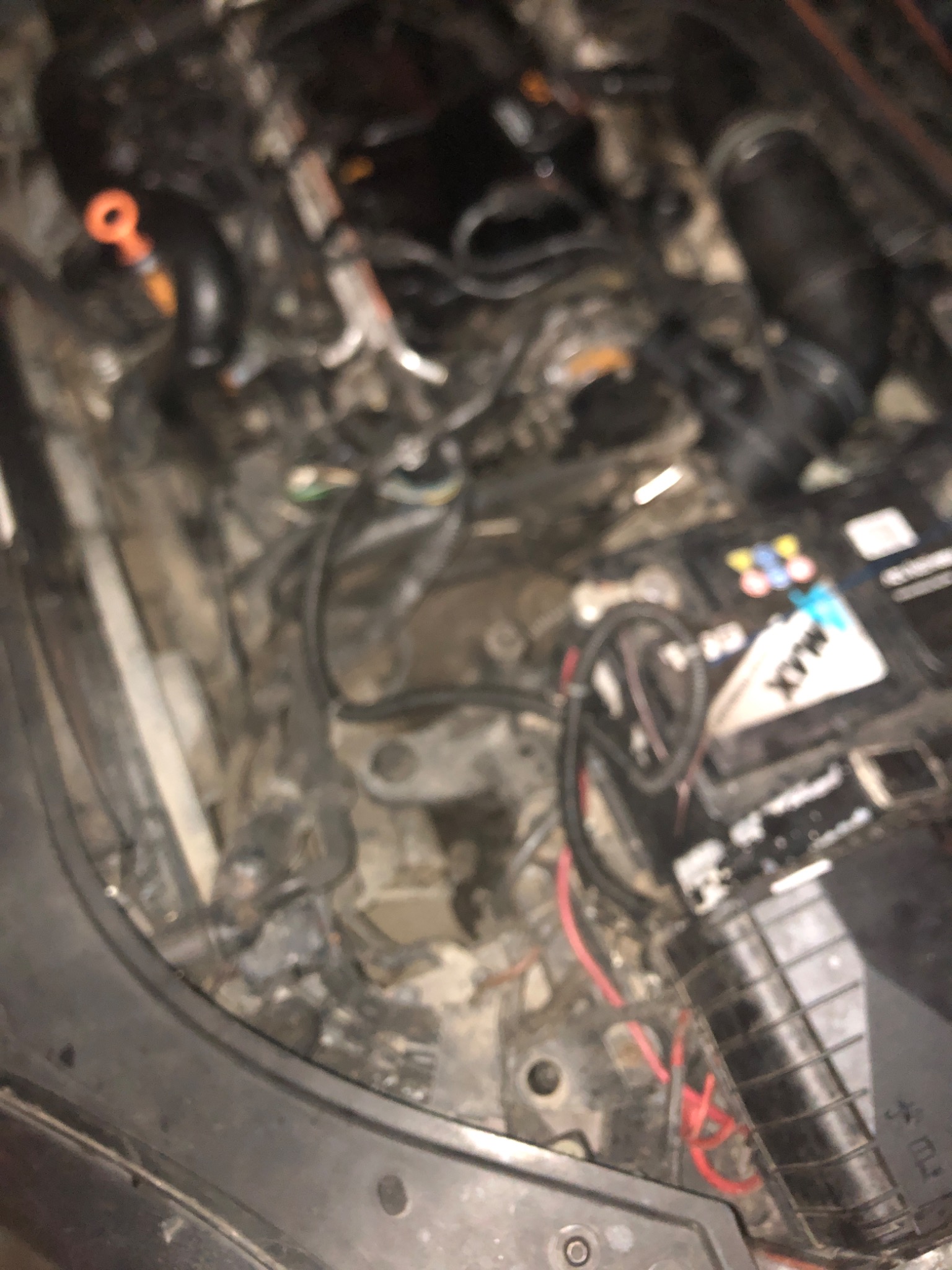 Niejasne ujęcie wnętrza brudnej komory silnika samochodowego z widocznymi przewodami, akumulatorem i wskaźnikiem poziomu oleju.