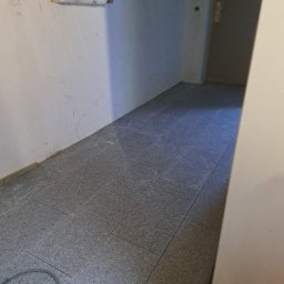 P.P. GRANIT PAWEŁ PRZĘCZEK - Szare płytki podłogowe w korytarzu, widoczne czerwone kliny dystansowe między płytkami, ściany przygotowane do malowania, widoczne kable elektryczne.