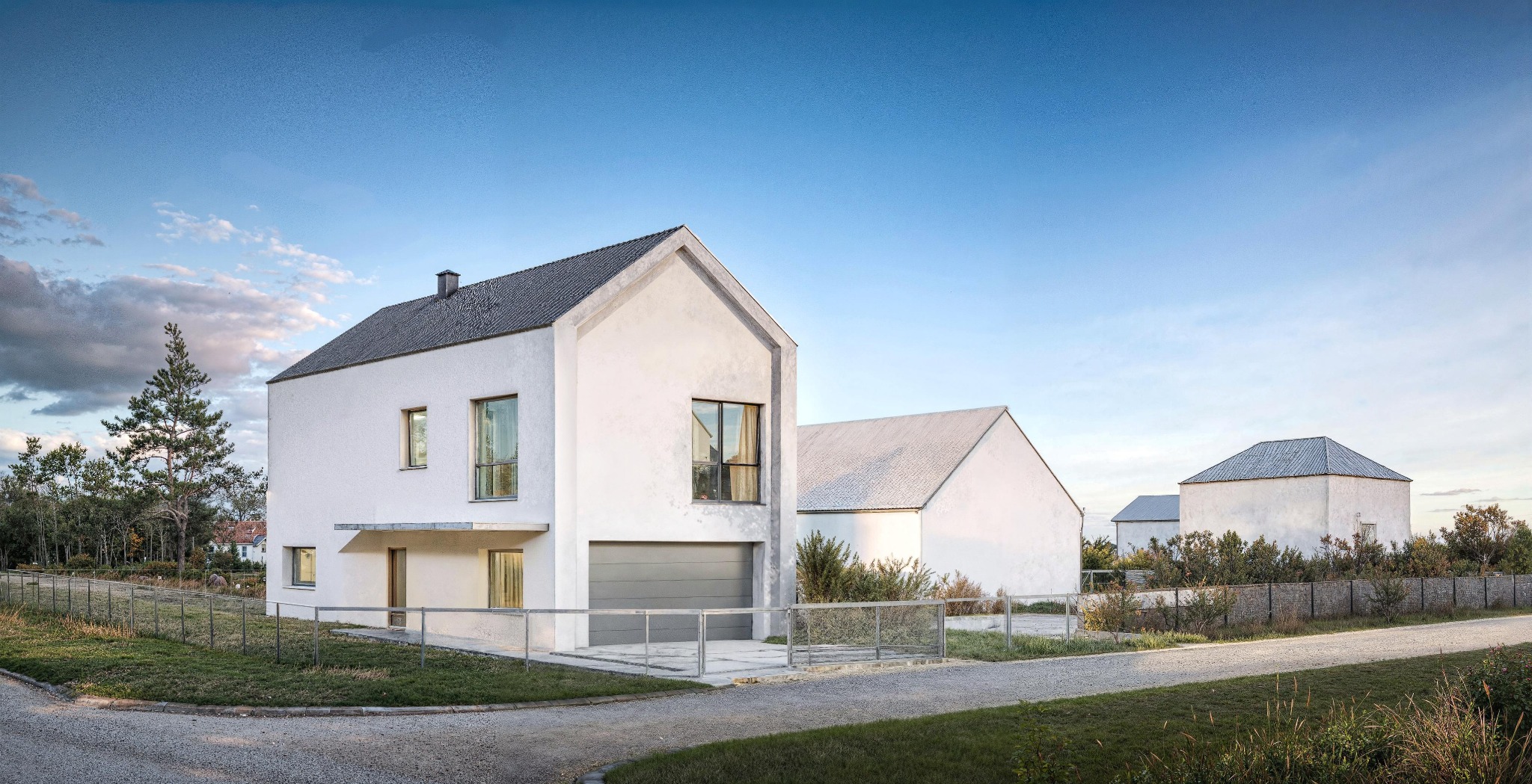 Wizualizacja nowoczesnego, białego domu z garażem i szarym dachem. Minimalistyczny styl, jasne tło nieba, metalowe ogrodzenie, widok z poziomu gruntu.