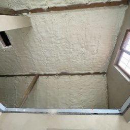 PROFI-PUR IHOR VOLKOV - Poddasze po natrysku izolacji. Widoczne drewniane elementy konstrukcyjne i okno dachowe. Izolacja pokrywa całą powierzchnię, tworząc jednolitą warstwę.