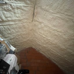 PROFI-PUR IHOR VOLKOV - Poddasze po natrysku izolacji piankowej, widoczne cegły i kartony. Izolacja pokrywa skośny dach, tworząc jednolitą warstwę. Detal wykończenia izolacji.