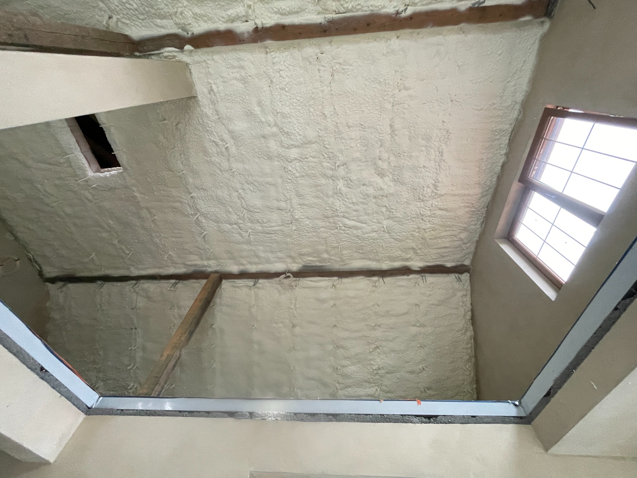 Poddasze po natrysku izolacji. Widoczne drewniane elementy konstrukcyjne i okno dachowe. Izolacja pokrywa całą powierzchnię, tworząc jednolitą warstwę.