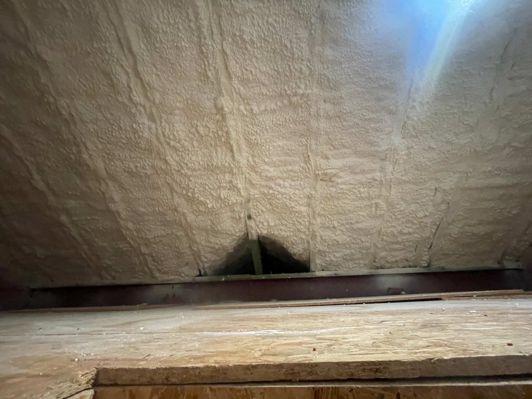 Ocieplenie poddasza pianką natryskową, widok z dołu. Widoczna drewniana konstrukcja i równomierna warstwa izolacji w kolorze kremowym.