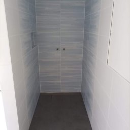 Numer 1 Remonty - Wykończony prysznic typu walk-in z szarymi płytkami imitującymi drewno na ścianach i ciemnoszarą podłogą, widoczne dwa zawory na ścianie.
